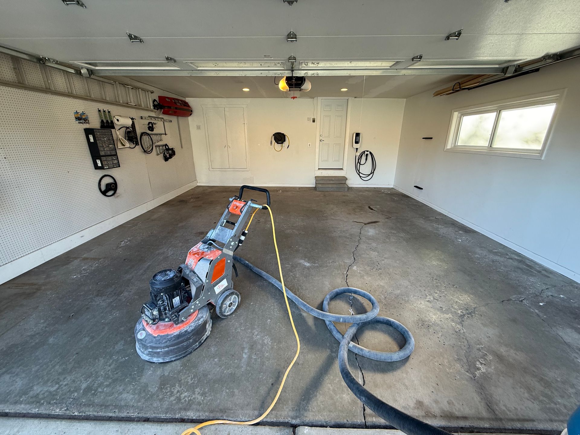 Person sanding a concrete garage floor with a floor grinder and vacuum hose.
