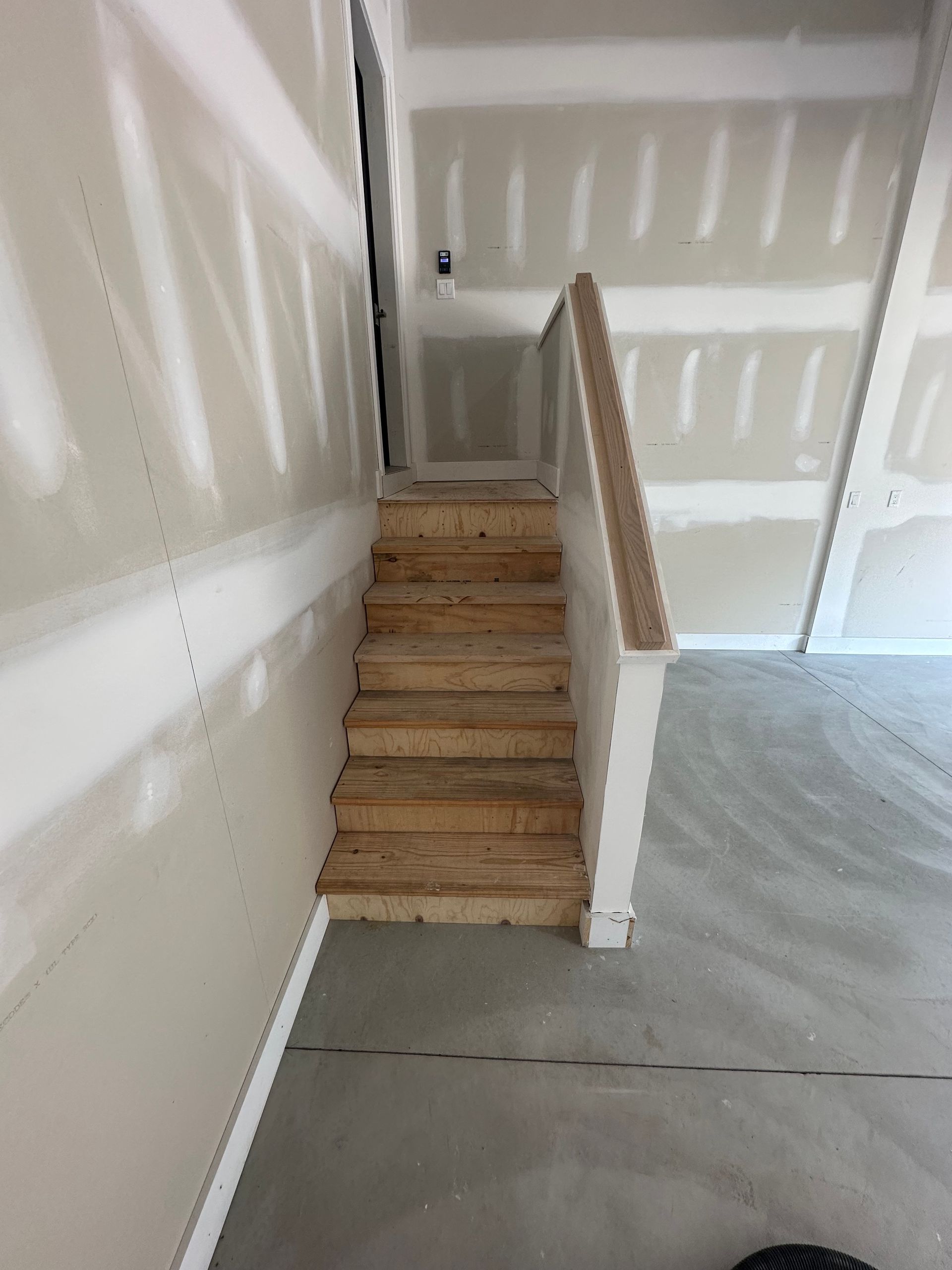 Indoor stairs leading to a small landing in an unfinished room with drywall and concrete floor