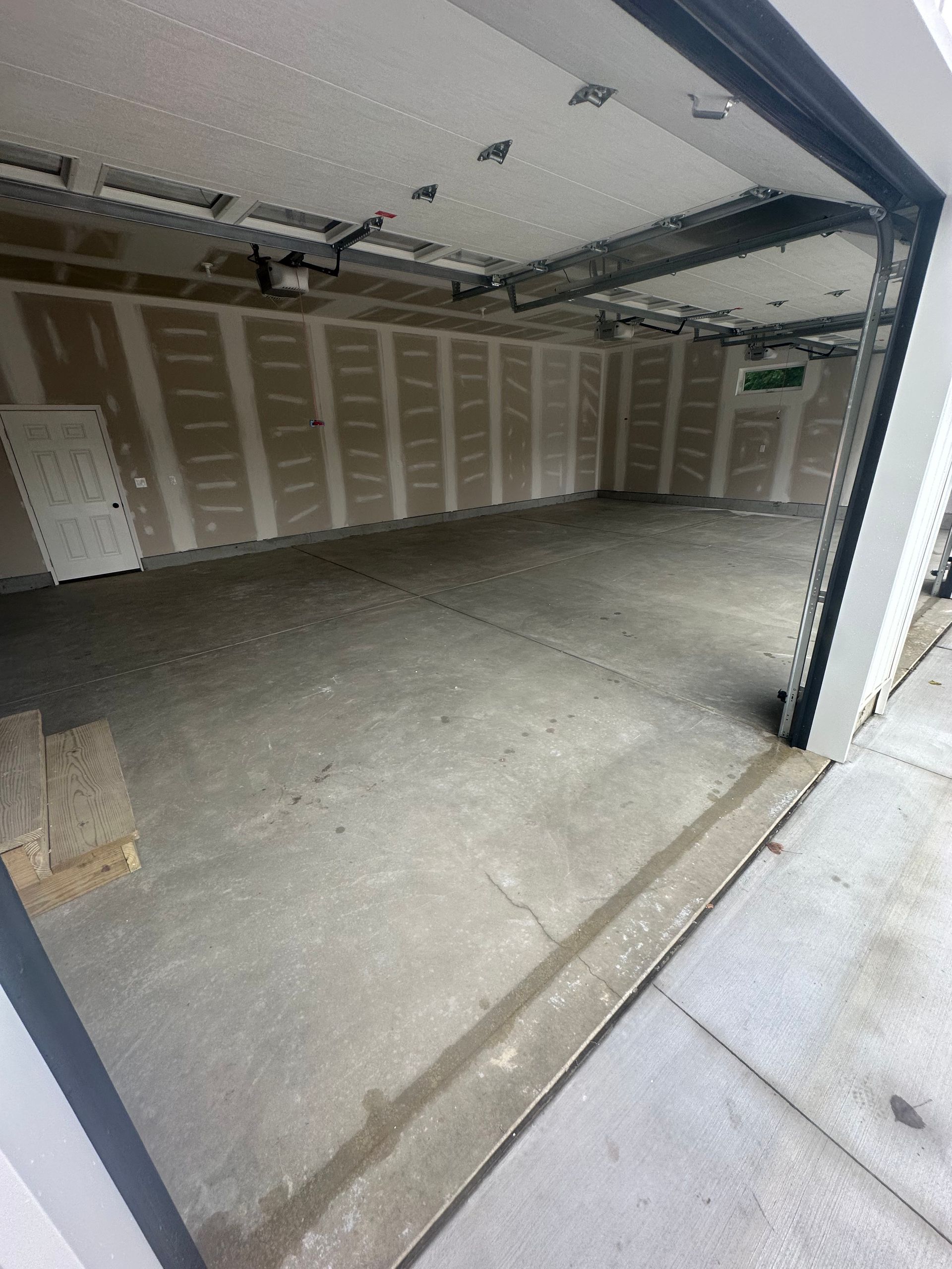 Empty unfinished garage interior with drywall, concrete floor, and open garage door