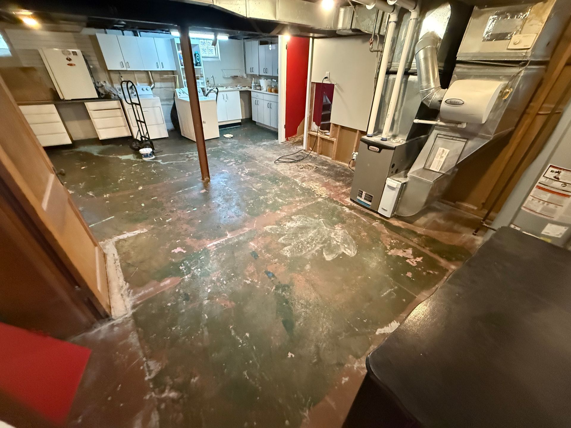 Basement utility room with exposed pipes, water damage, and a wet floor