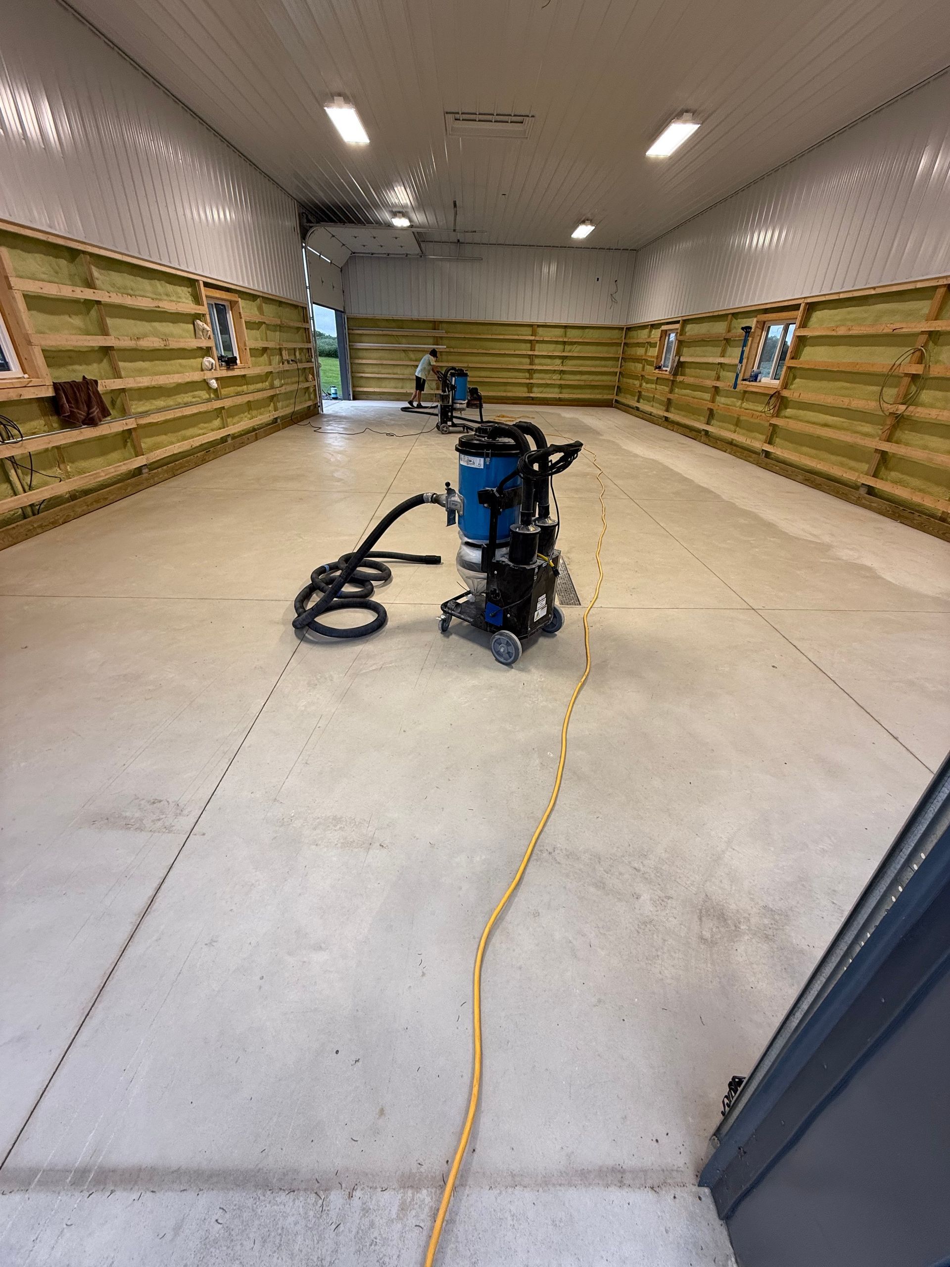 Large empty warehouse with stacked wooden shelves and a blue floor scrubber in the center, hose on concrete floor