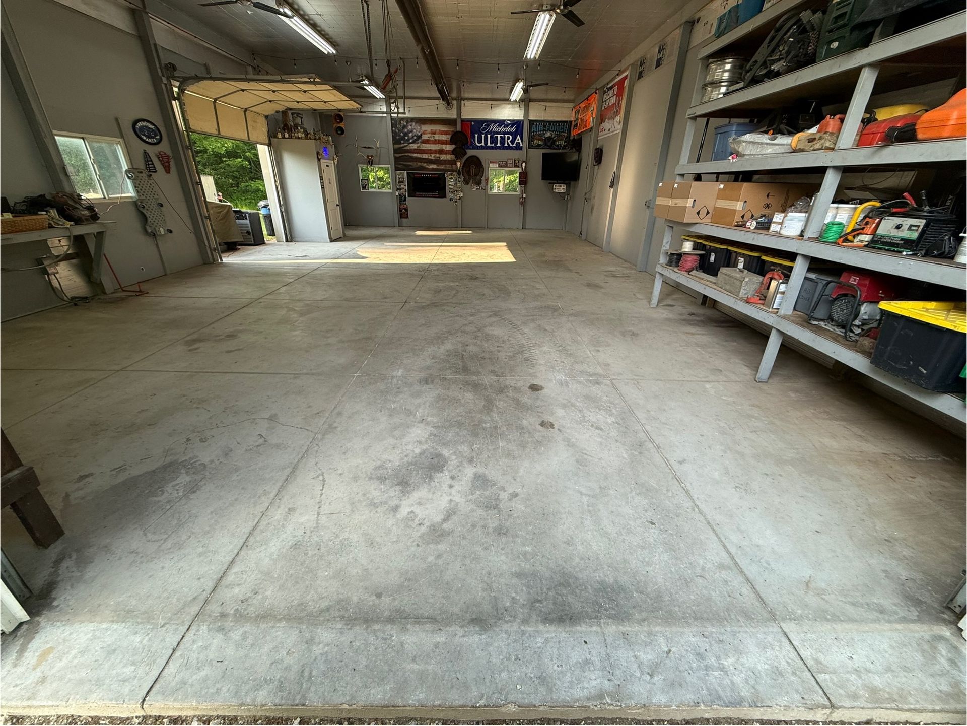 Empty garage interior with concrete floor, shelves along the right wall, and an open doorway to daylight.