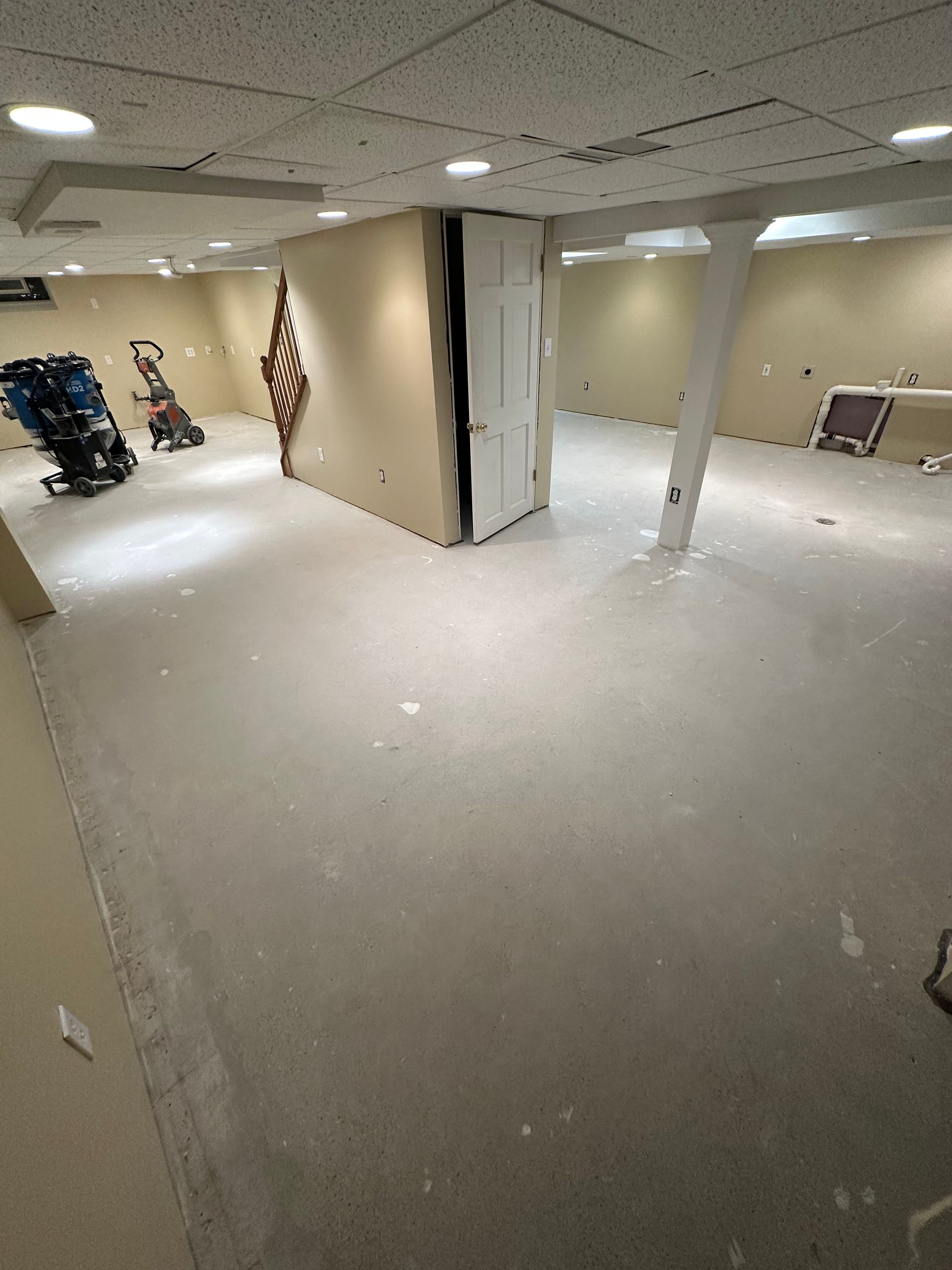 Empty office space with beige carpet, white walls, support columns, and an American flag by the wall.