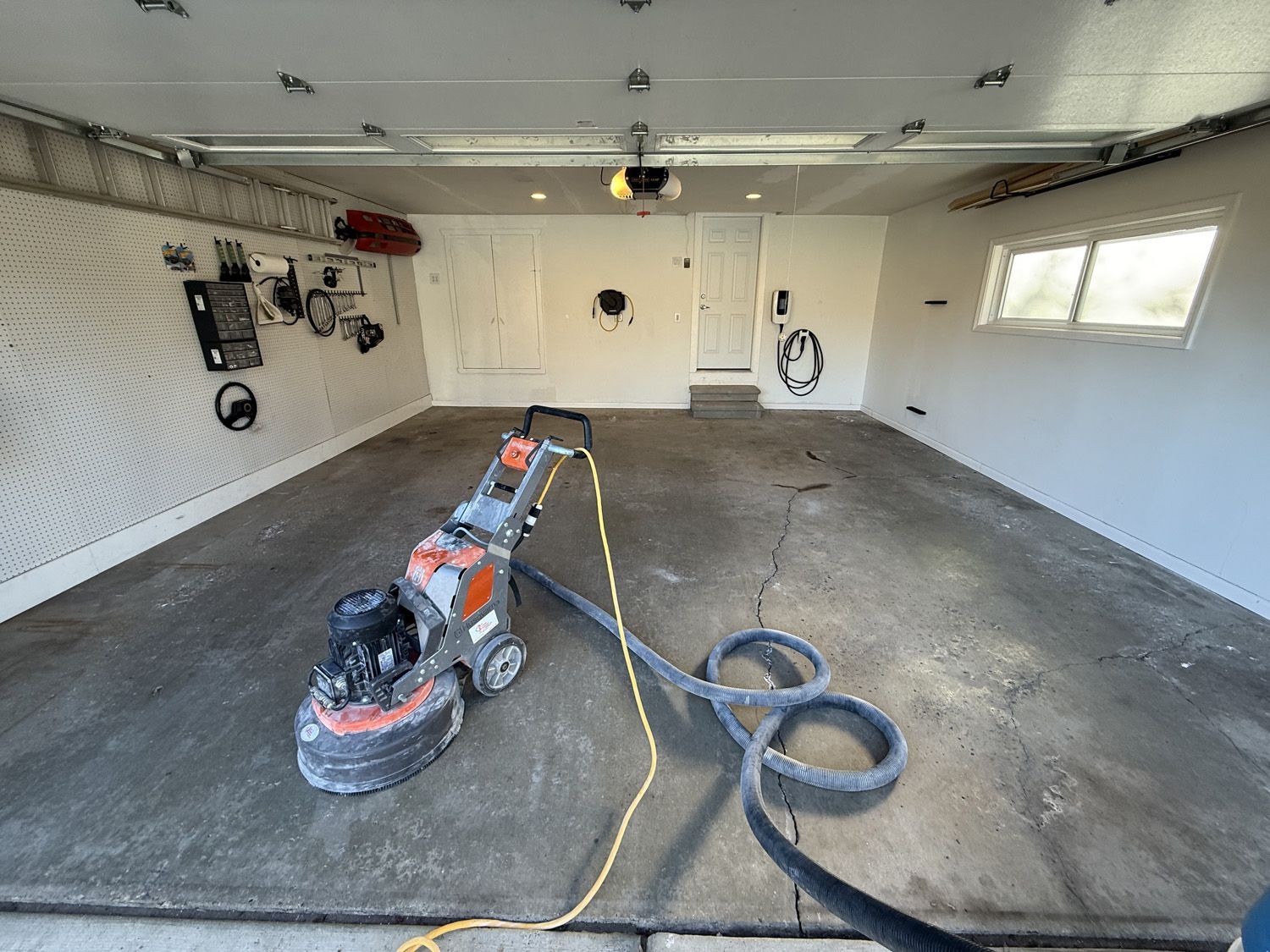 Garage floor being sanded with a floor sander and dust hoses attached
