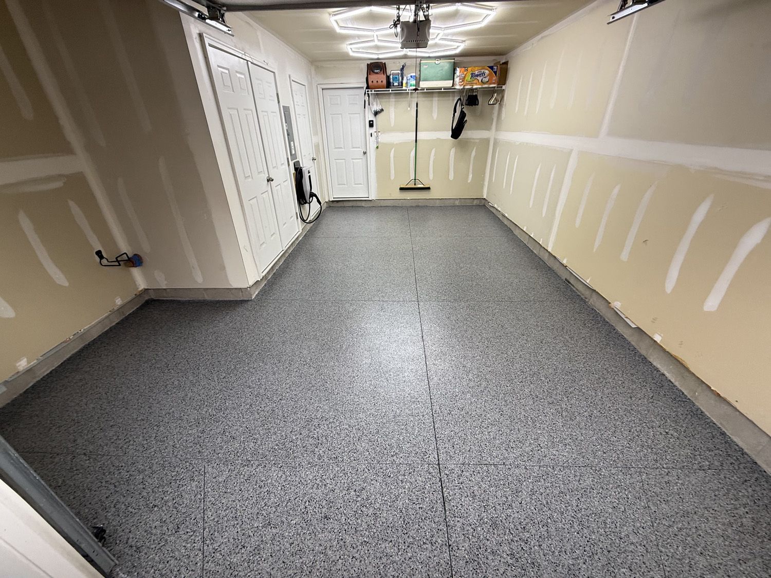 Empty garage with gray speckled floor, beige walls, and storage shelves at the back.