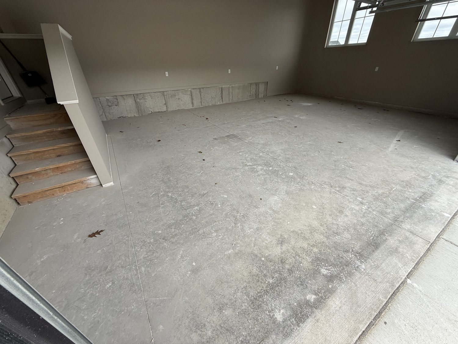 Empty unfinished room with concrete floor, staircase on the left, and a small window on the right.