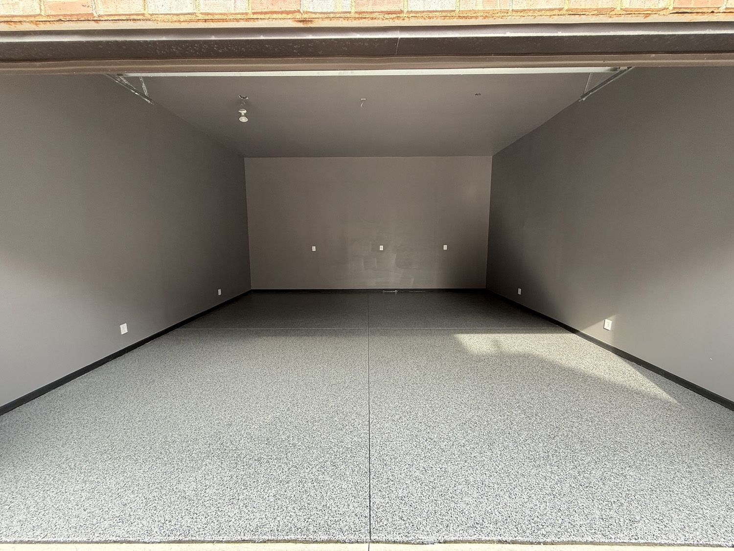 Empty gray garage interior with speckled floor and open doorway view