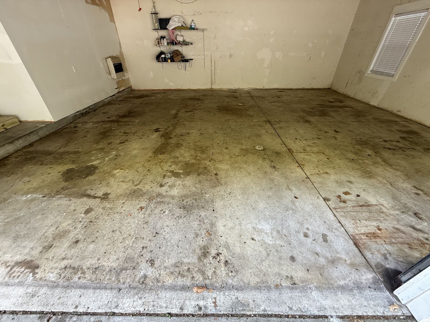 Empty unfinished room with stained concrete floor and white walls, showing damage and utility cutouts.