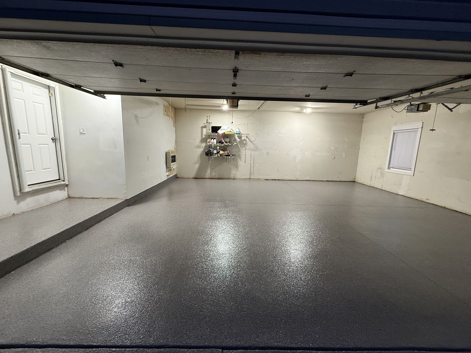 Empty gray room with glossy floor, white walls, and low ceiling, resembling a garage or basement.