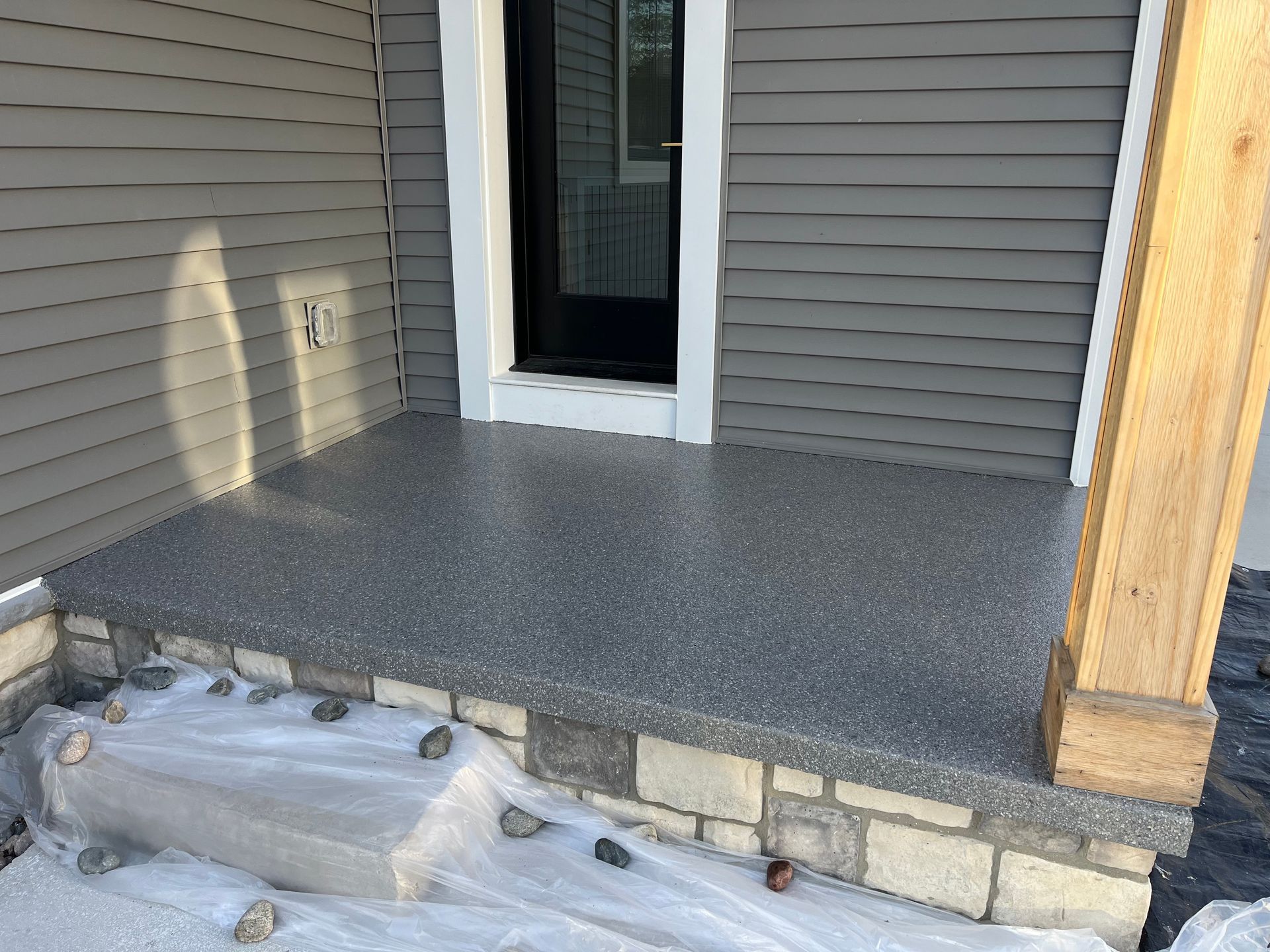 Front porch with gray siding, dark speckled floor, stone steps, and a wooden post under construction