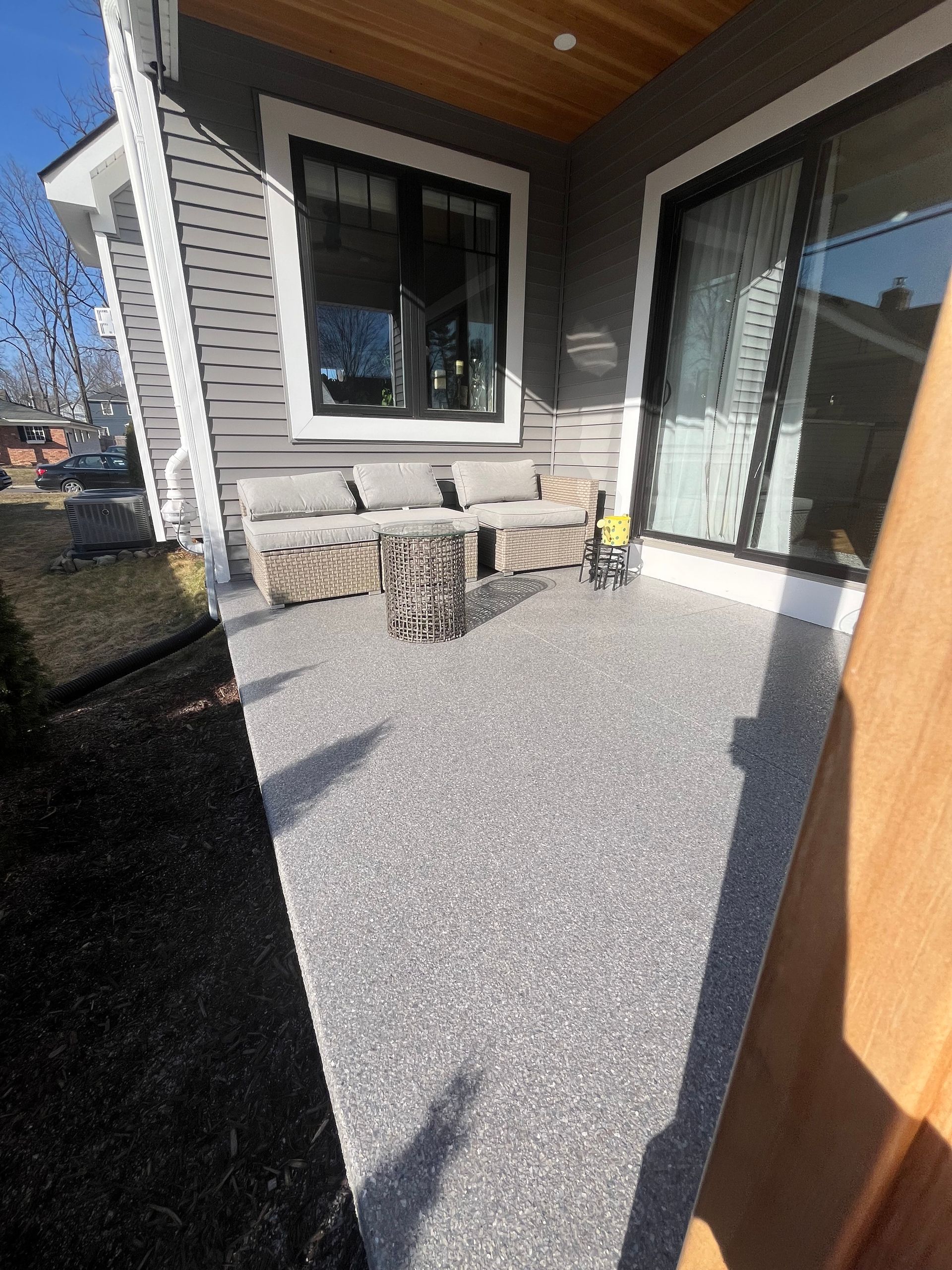 Small covered patio with gray pebble flooring, stone wall, black-framed window, and sliding glass door.
