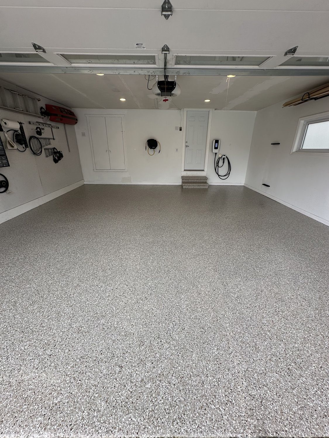 Empty garage with speckled epoxy floor, white walls, and overhead storage equipment.