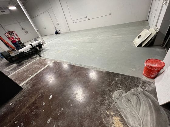 A large empty room with a bucket of paint on the floor.