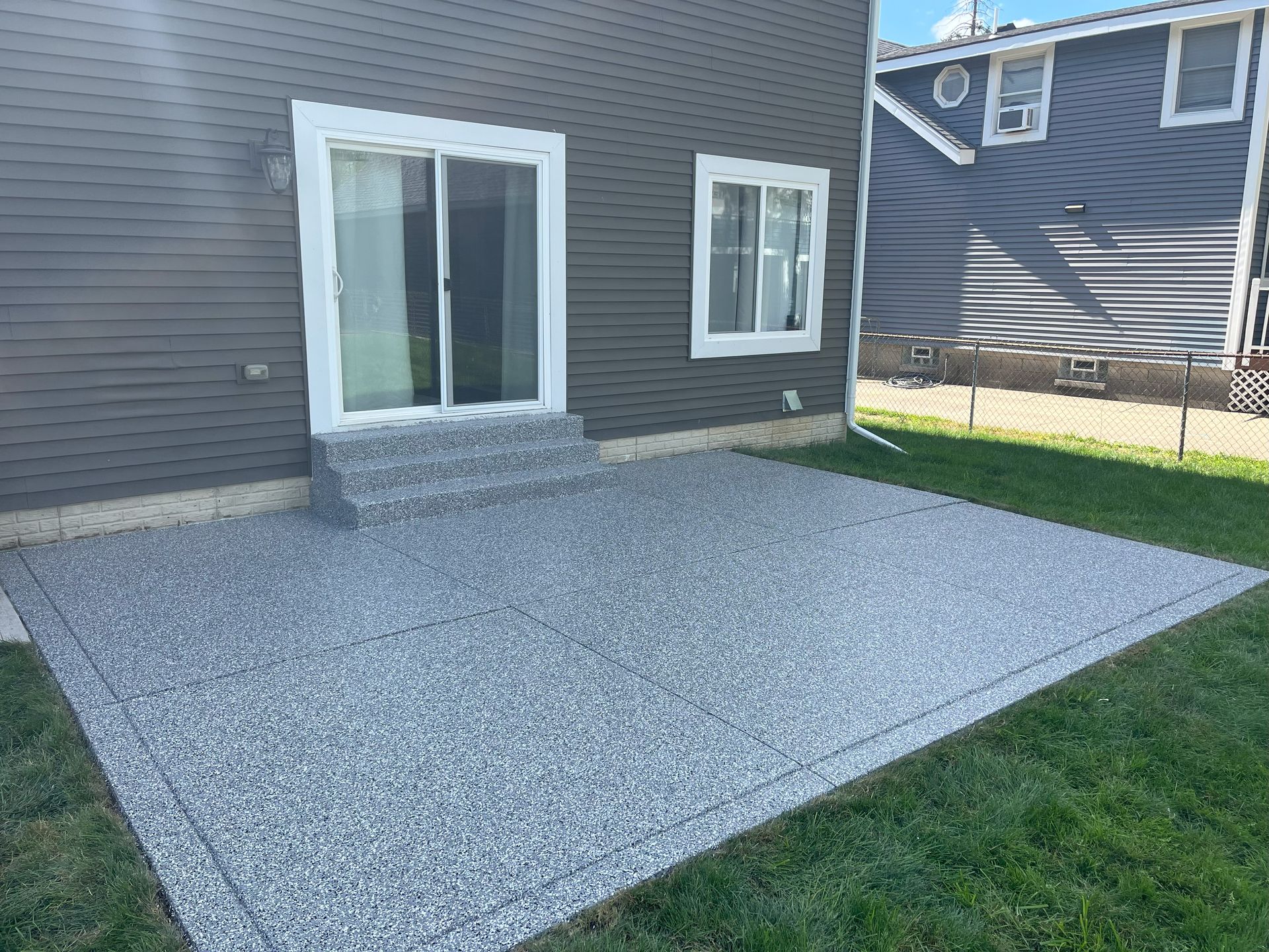 Gravel patio beside a dark gray house with two white-framed windows and a sliding glass door.