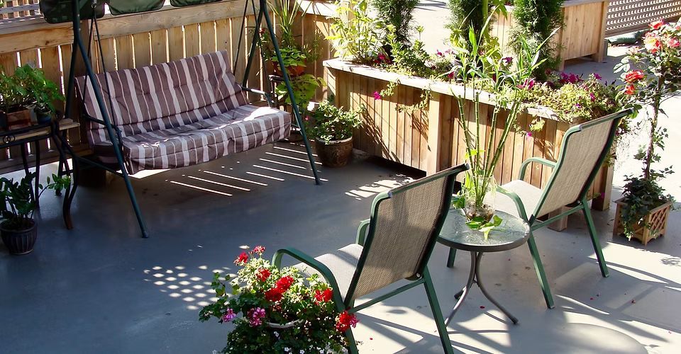A patio with a swing and chairs and flowers