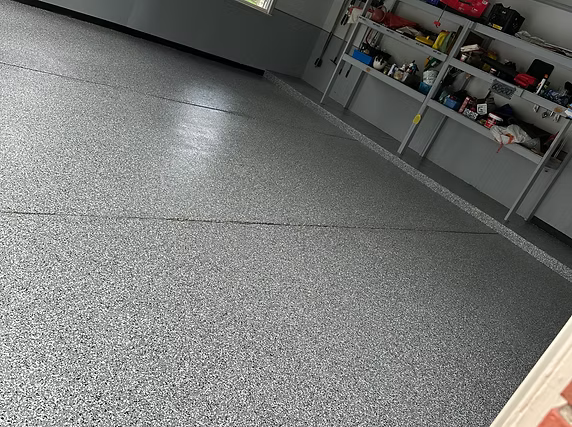 A garage with a gray floor and shelves filled with tools.