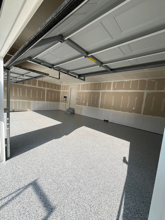 An empty garage with a garage door open and a shadow on the floor.
