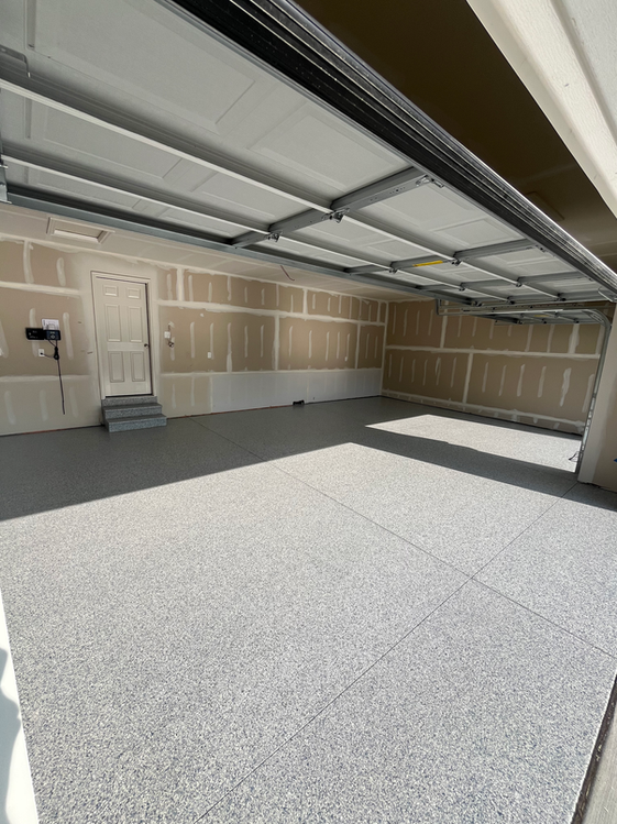 An empty garage with a garage door open and a gray floor.
