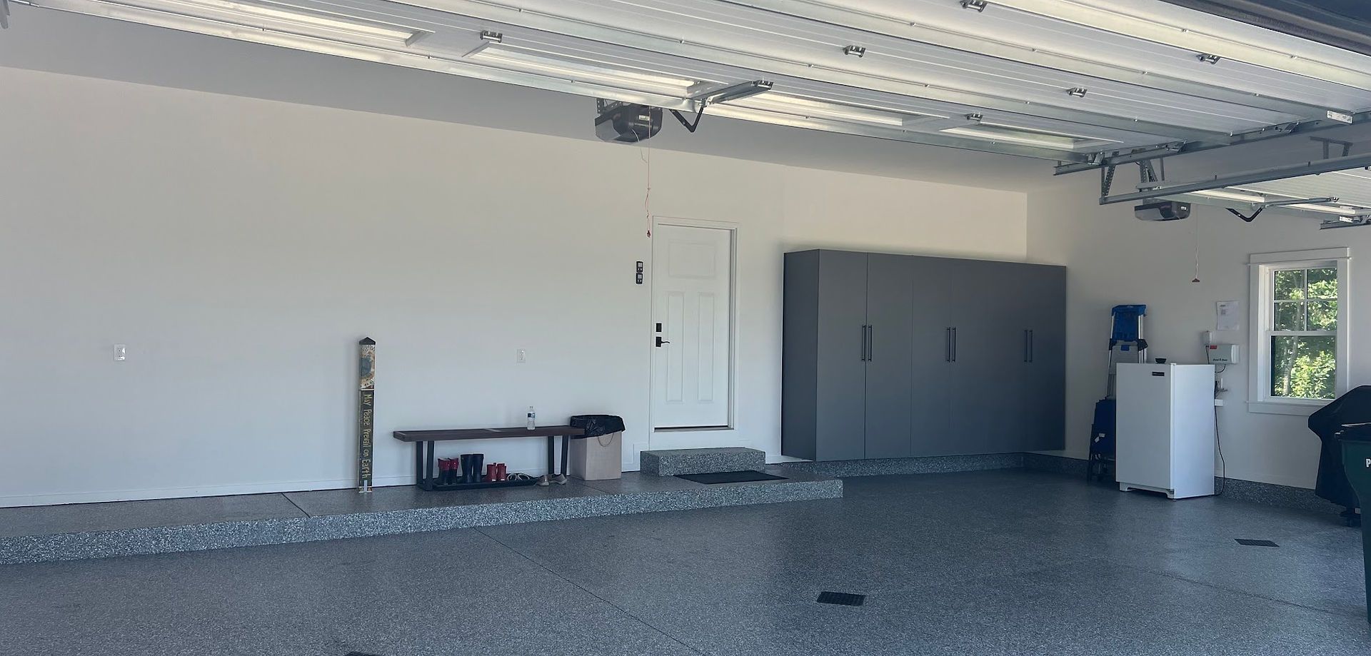 Empty garage interior with gray floor, white walls, overhead lighting, and closed doors.