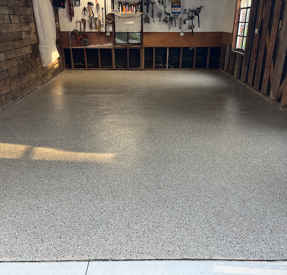 Empty gray epoxy floor in a workshop or garage, with exposed wooden walls and storage shelves at the back