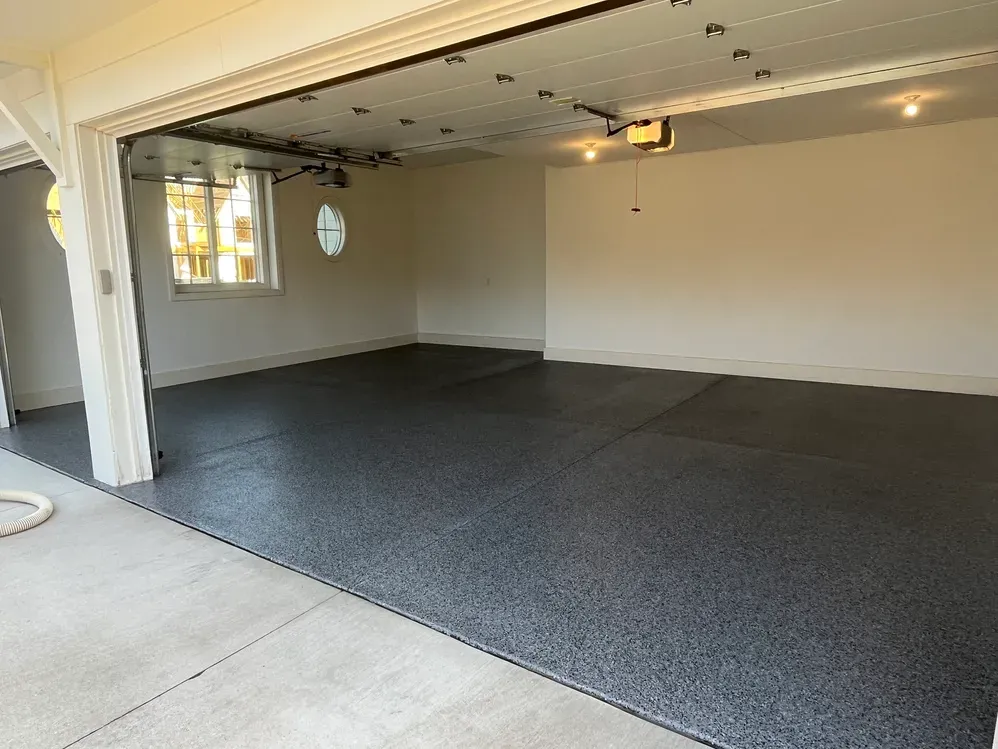 An empty garage with a black floor and a garage door open.