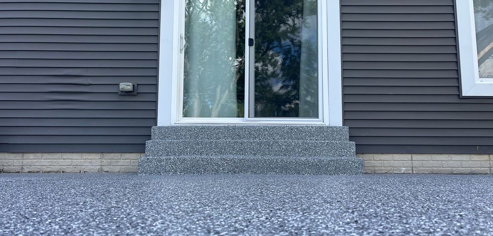 House entrance with glass double doors, gray siding, and a pebble-textured front step.