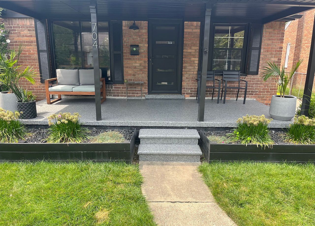 Brick house front porch with black door, stone steps, seating, and a walkway across the lawn