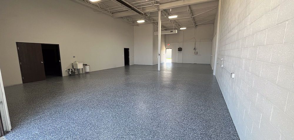 Empty industrial warehouse interior with speckled floor, white walls, and high ceiling lights