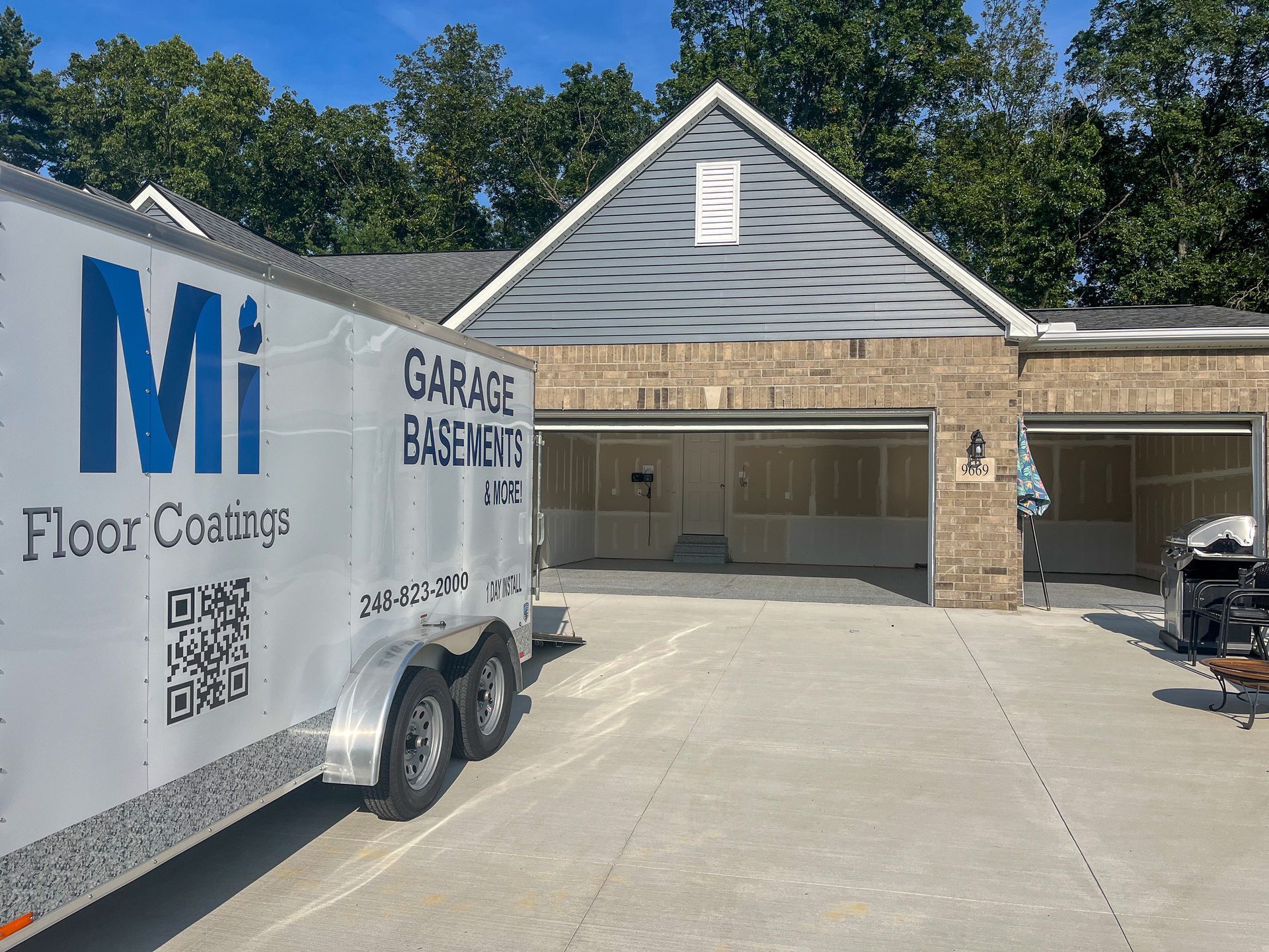A white trailer is parked in front of a brick house.