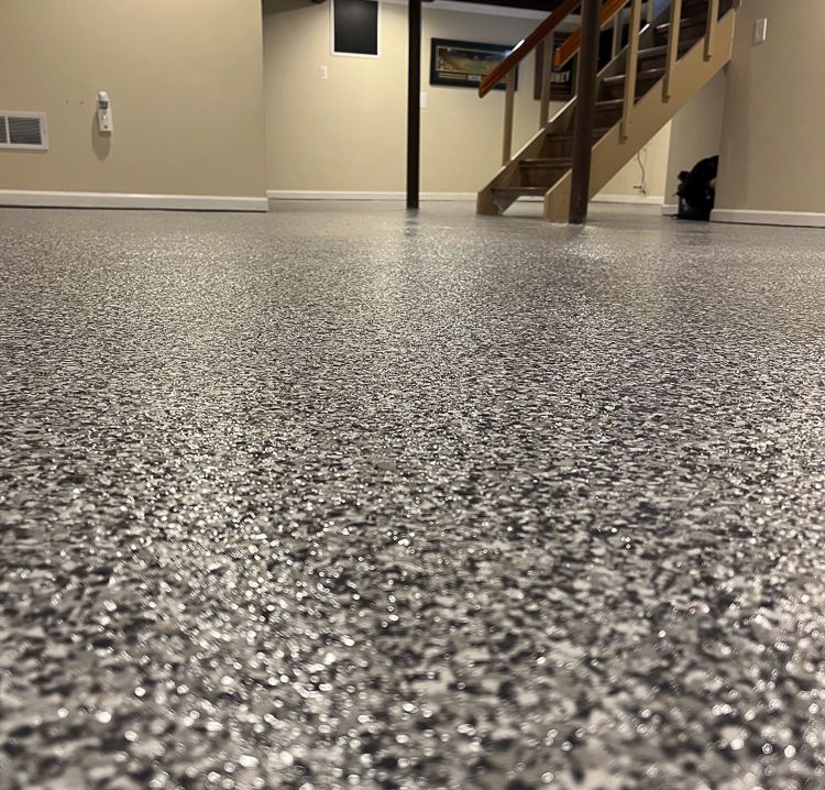 Low-angle view of a speckled epoxy floor in a hallway with stairs and beige walls in the background