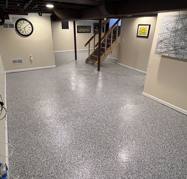 Basement room with speckled floor, staircase, wall clock, and framed artwork.