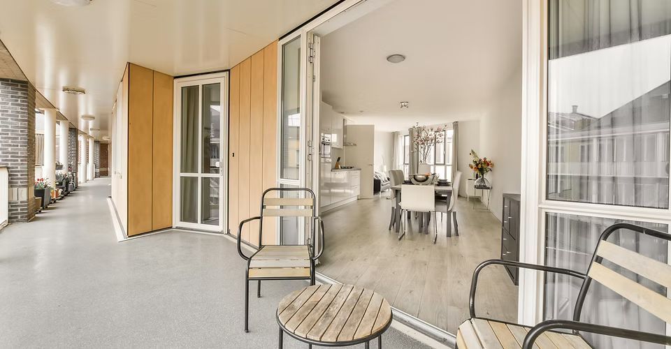A balcony with chairs , a table and a dining room in the background.