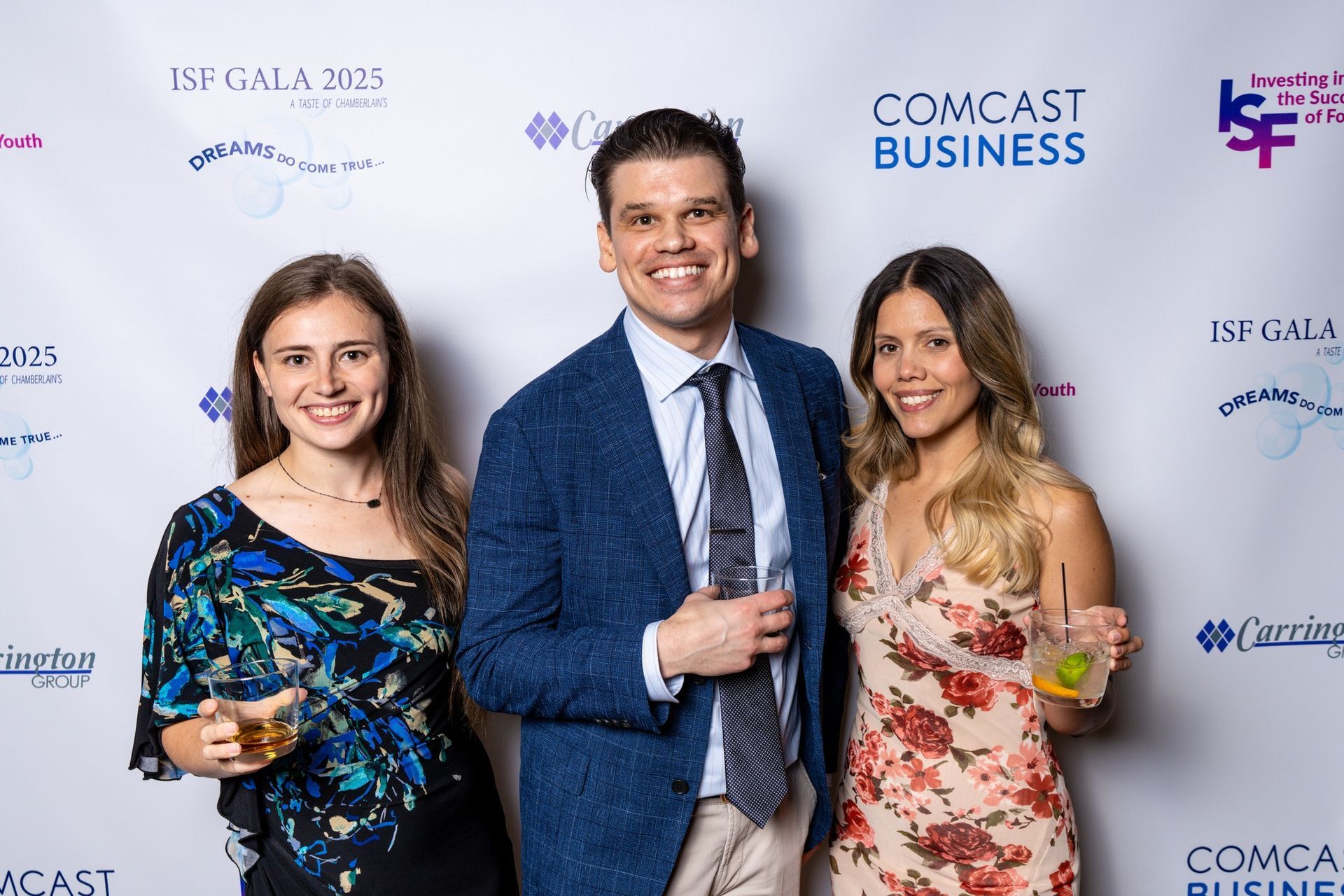 Three people posing at a Comcast Business event backdrop, smiling and holding drinks.