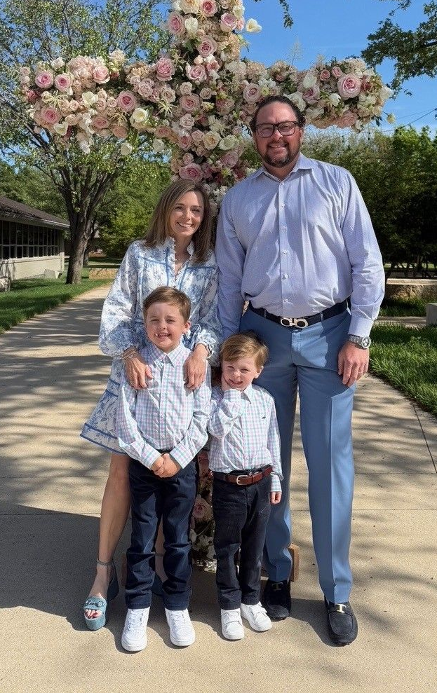 Family of four standing on a sidewalk under blooming pink trees on a sunny day