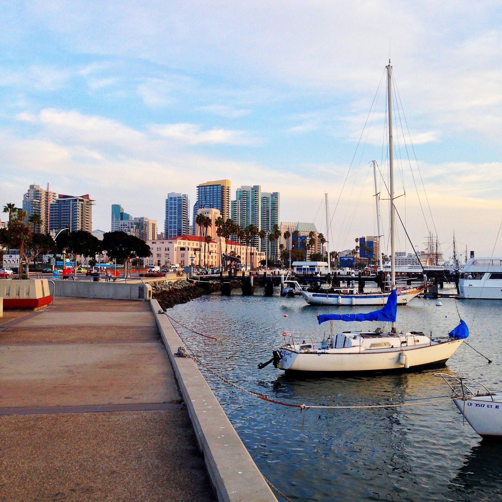 Harbor marina with sailboats, waterfront promenade, and city buildings at sunset