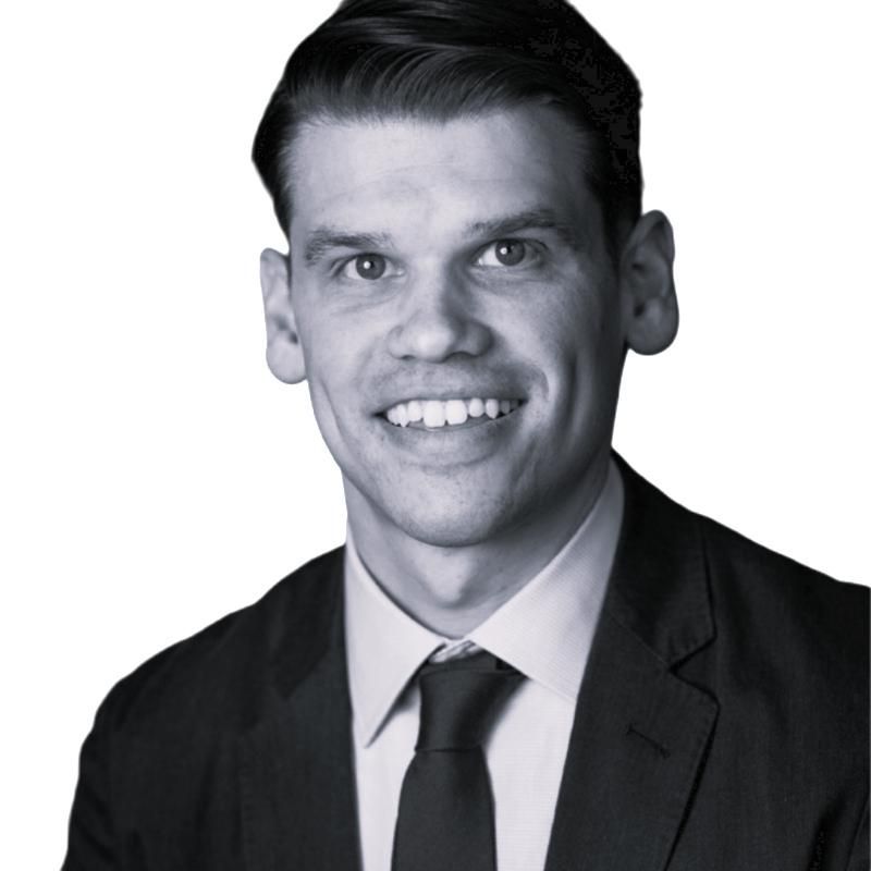 Studio portrait of a smiling man in a dark suit and tie against a plain background