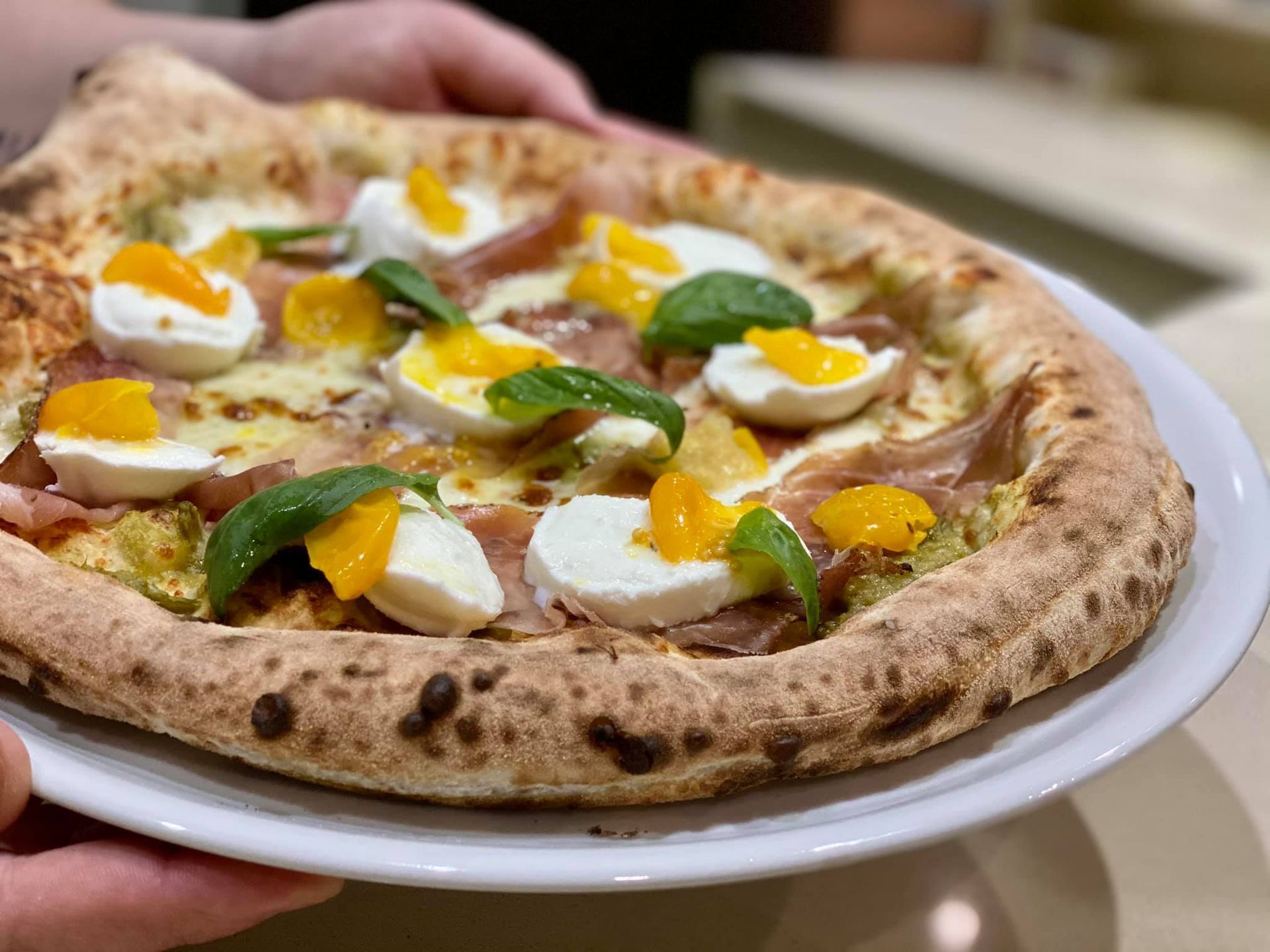Pizza con prosciutto, mozzarella, fette d'arancia e basilico su un piatto bianco.