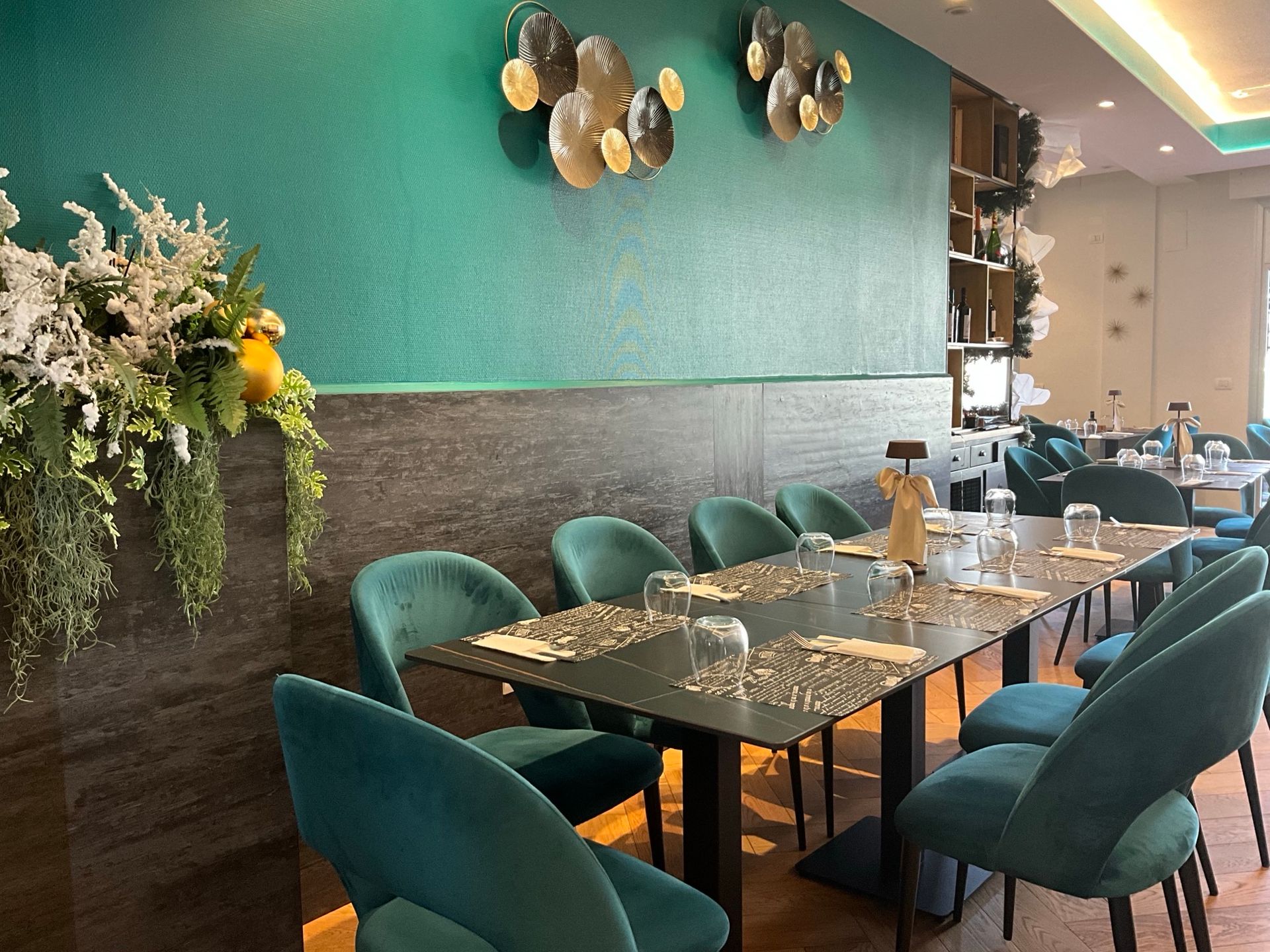 Elegante interno del ristorante con sedie in velluto verde acqua, tavolo scuro e parete verde con decorazioni dorate.