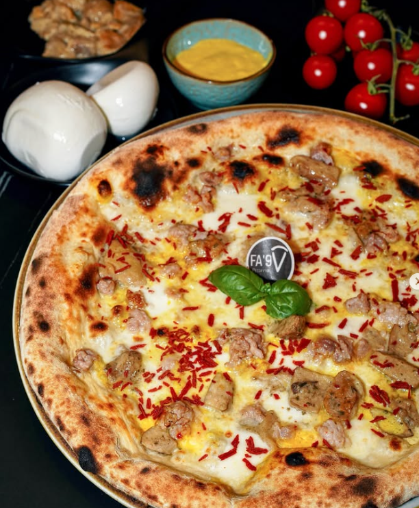 Pizza con salsiccia, formaggio e fiocchi rossi, con contorno di salsa, pomodori e cipolle.