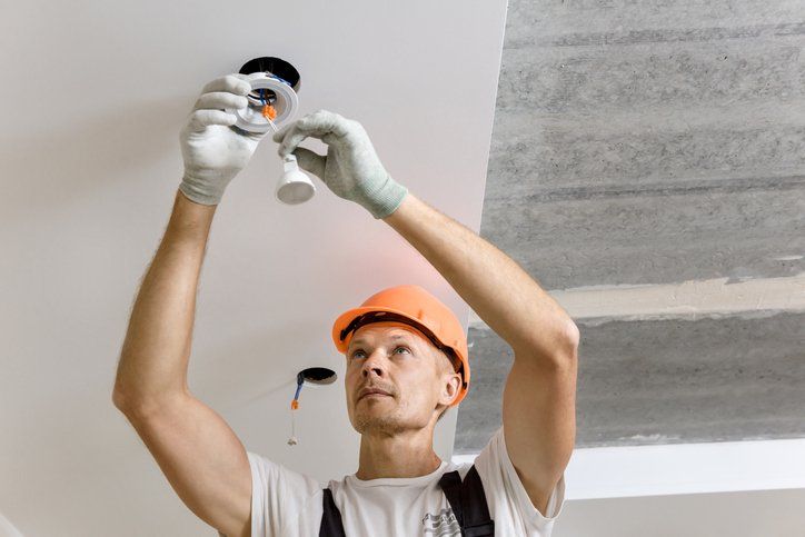 The electrician is installing LED spotlights on the ceiling