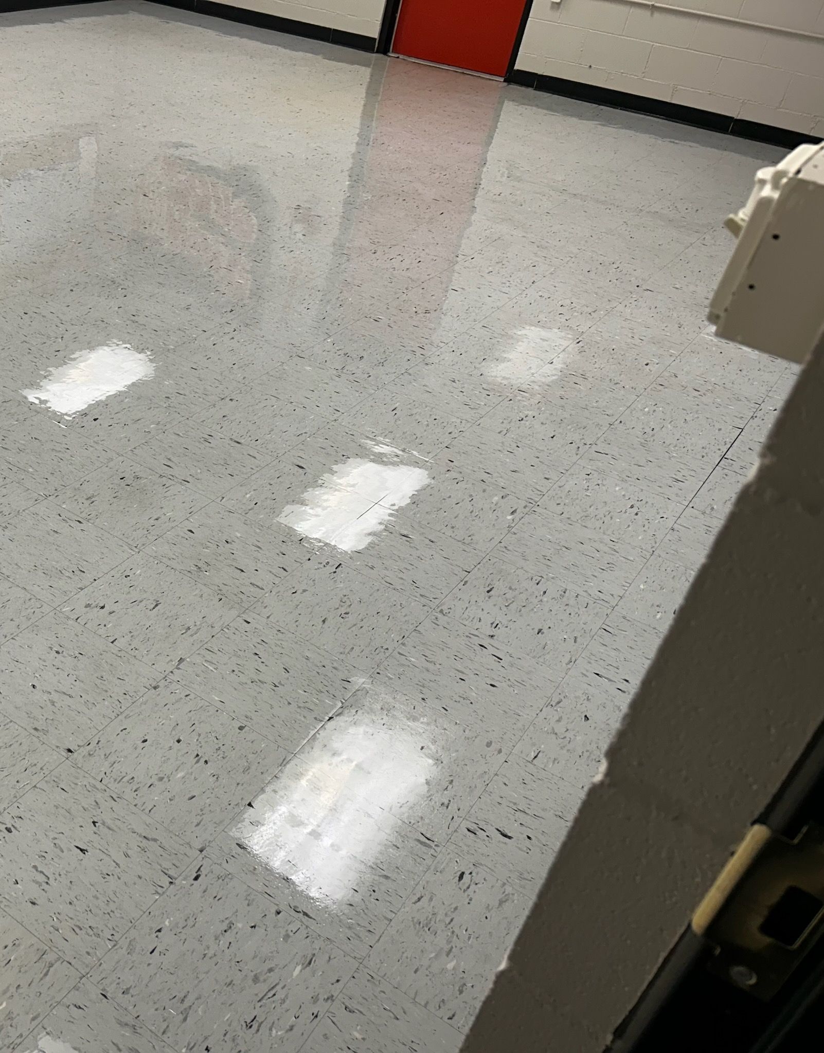 A high-angle view of a gray, speckled garage floor with four distinct, rectangular white patches or repairs.