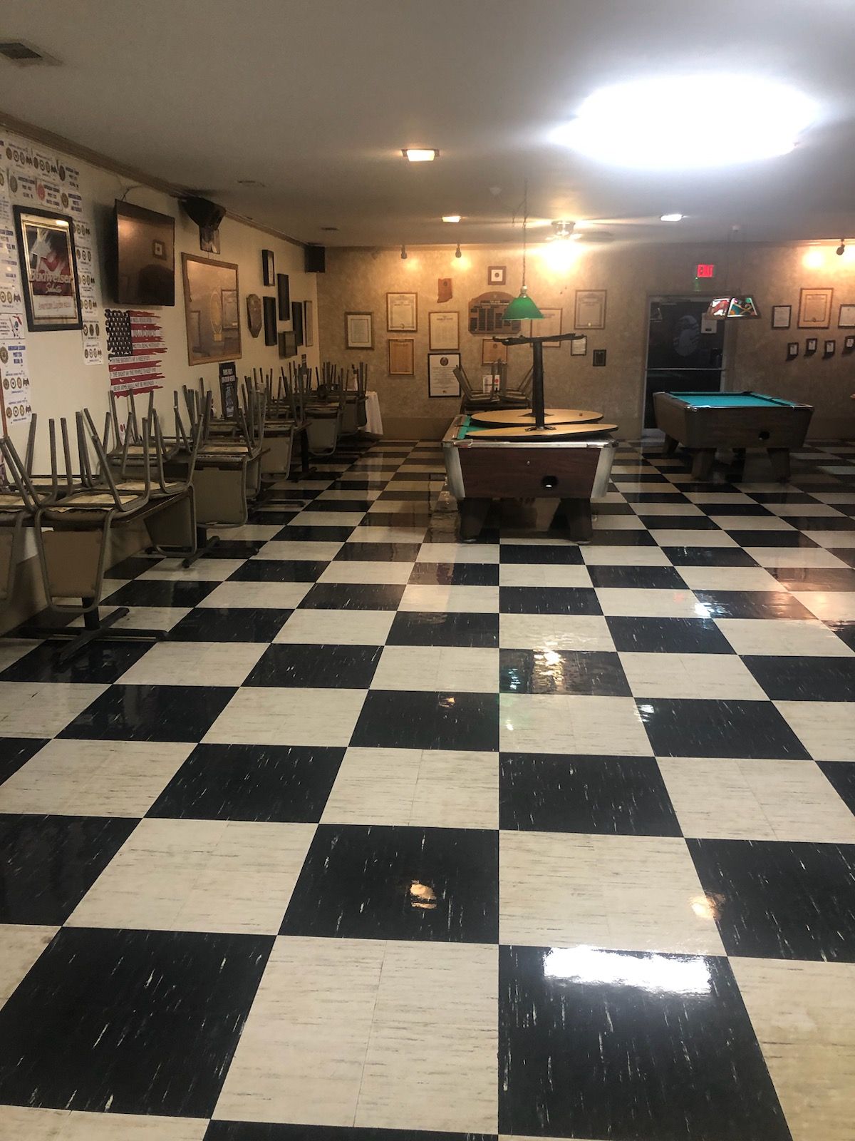 Empty community hall with a black-and-white checkered floor, billiards tables, and chairs stacked on tables.