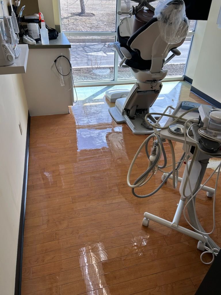 A dental exam room with a flooded, glossy floor, a dental chair, and medical equipment under a large window.