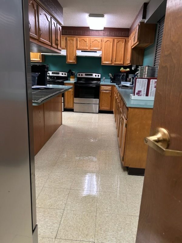 View through a doorway into a kitchen with honey-oak cabinets, green countertops, and light tile flooring.