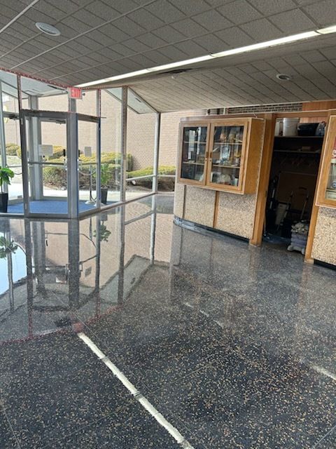 A lobby with polished dark granite floors, a glass revolving door, and a wooden display case along the wall.