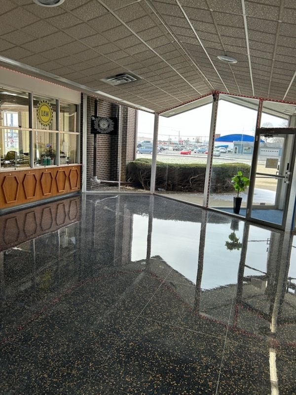 A bright, modern lobby with polished dark gray speckled flooring, a wood-paneled reception desk, and floor-to-ceiling glass.