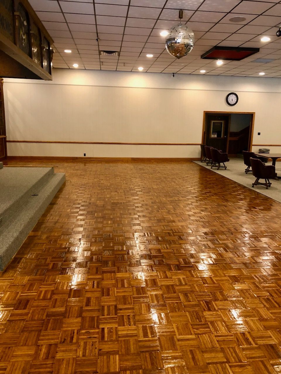 Empty dance floor with shiny, patterned wood floor, a stage, and disco ball.