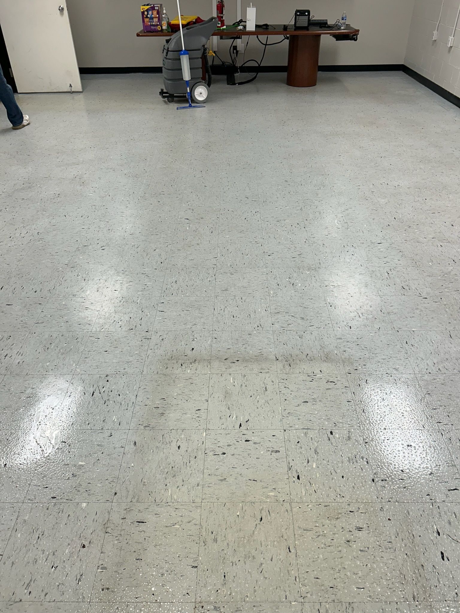 A polished, speckled floor in an office space, with a desk and some cleaning equipment in the background.