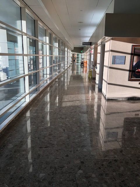 A long, empty indoor hallway with large glass windows on the left and reflective gray tiled flooring.