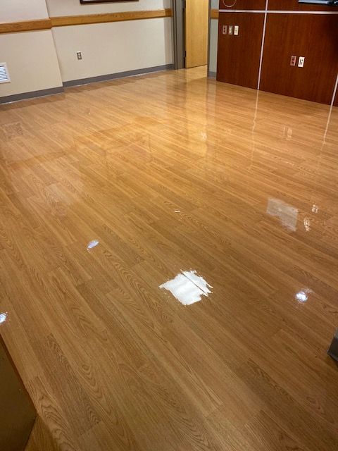 A bright, empty room with polished, light-brown wood flooring and warm-toned wood-paneled walls.